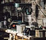 A detailed view of a cluttered workshop with a focus on a drill press and various tools.