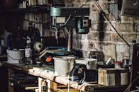 A detailed view of a cluttered workshop with a focus on a drill press and various tools.