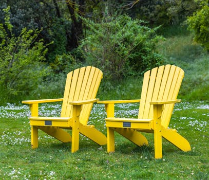 Two vibrant yellow Adirondack chairs in a green garden setting, perfect for relaxation.