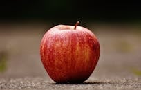 A vibrant red apple resting on a textured outdoor surface, showcasing natural beauty and freshness.