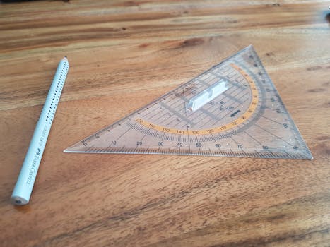 A clear triangle ruler and Faber-Castell pencil on a wooden desk, perfect for precision drawing.