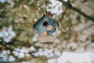 A decorative birdhouse adorned with floral motifs, set against a blurred, natural background.