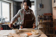 African American woman woodworking, applying glue in workshop setting. Focus on craftsmanship and woodworking tools.