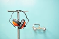 Close-up of earmuffs hanging on a metal stand in front of a teal wall.