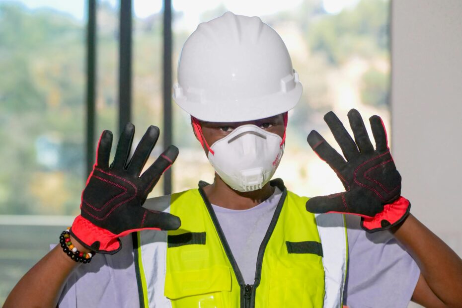 Construction worker wearing PPE gear including hardhat, gloves, and mask indoors.